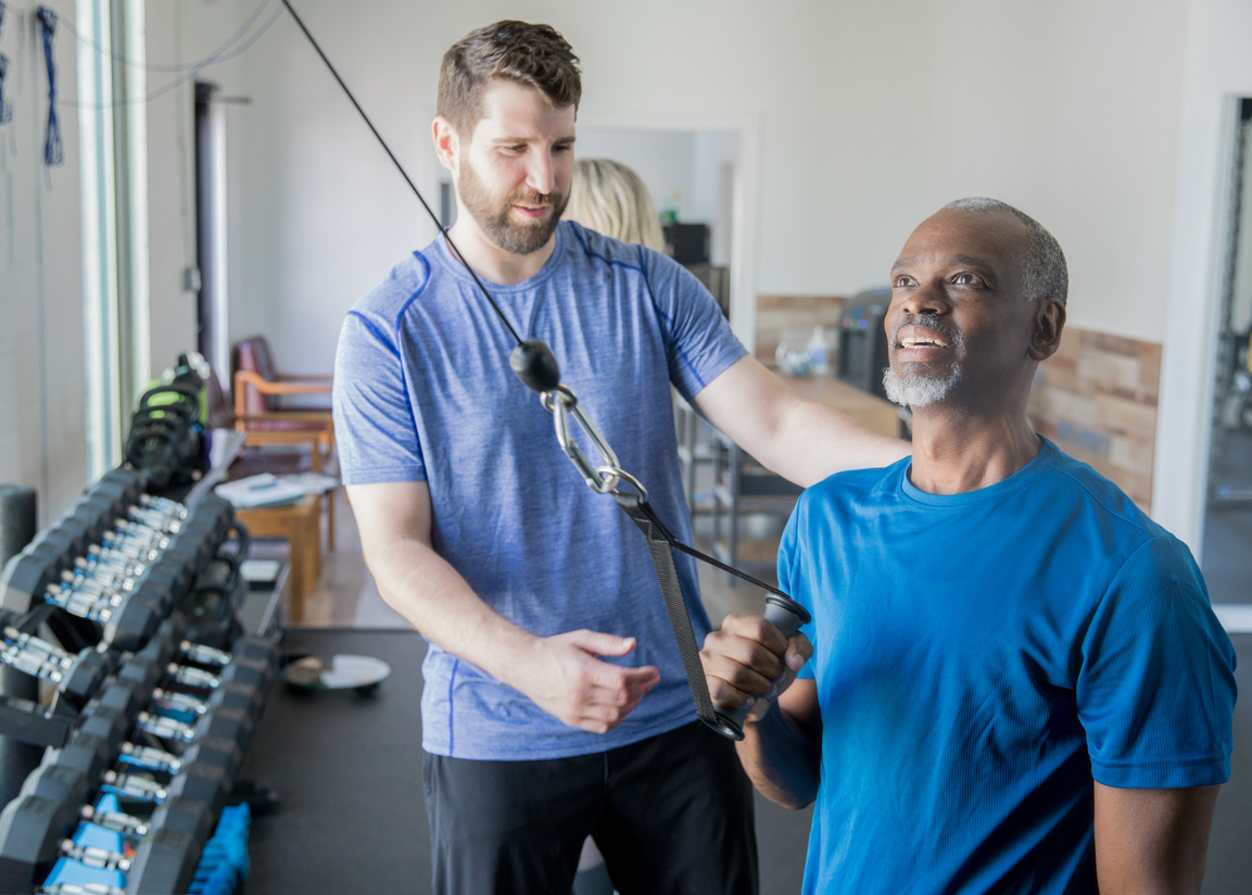 Personal trainer helping senior client with resistance weight training